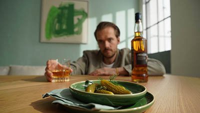 Мужчина пьет виски закусывая солеными огурцами
