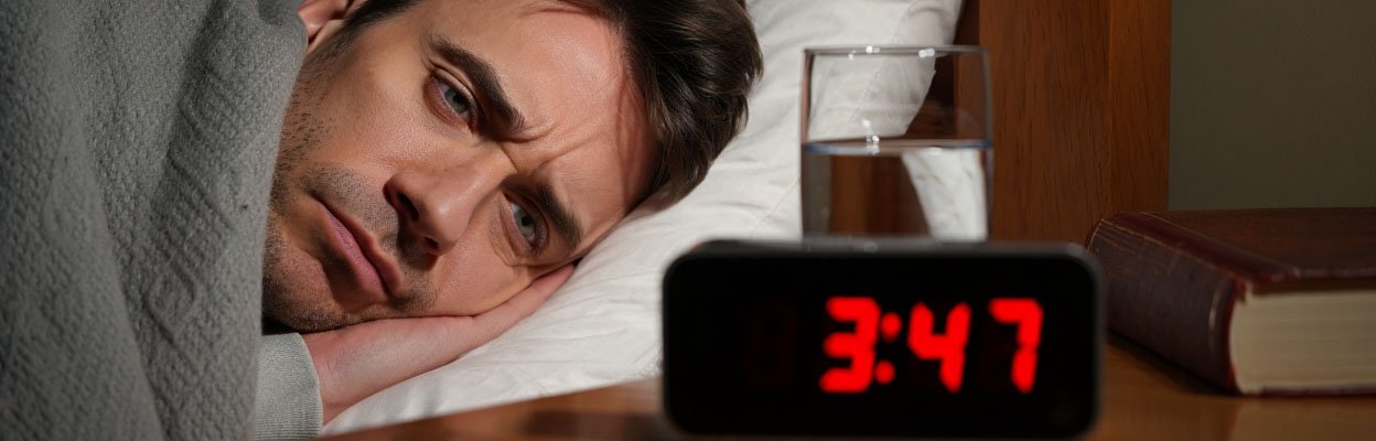 Мужчина лежит в кровати и смотрит на часы